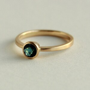 May include: A gold ring with a round, bezel-set, dark blue gemstone.