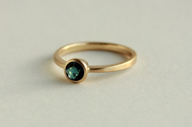 May include: A gold ring with a round, bezel-set, dark blue gemstone.
