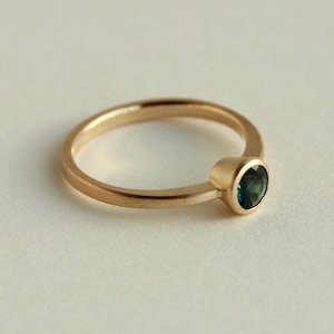 May include: A gold ring with a single round green gemstone.