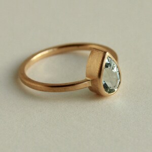 May include: A gold ring with a pear-shaped aquamarine gemstone set in a bezel setting.