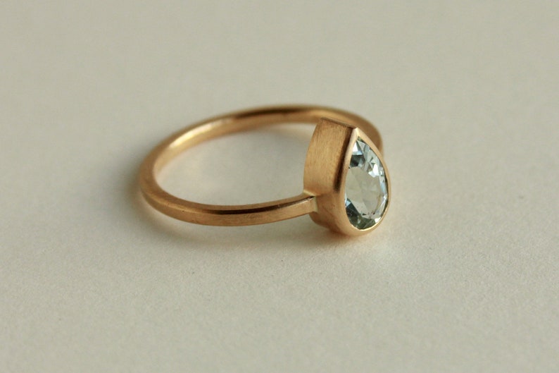 May include: A gold ring with a pear-shaped aquamarine gemstone set in a bezel setting.