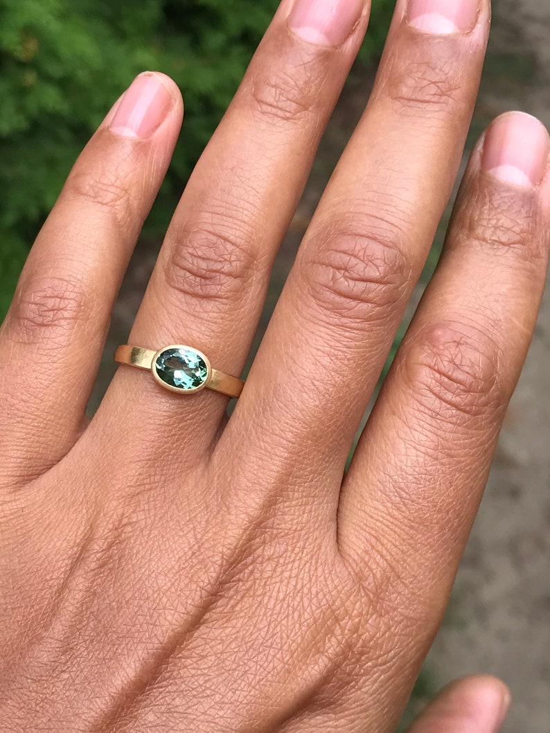 May include: A gold ring with a green oval gemstone set in a bezel setting.