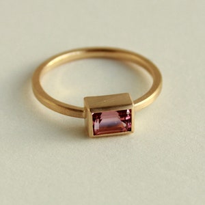 May include: A gold ring with a pink rectangular gemstone set in a gold bezel.