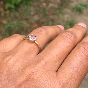May include: A gold ring with a round, light purple gemstone.