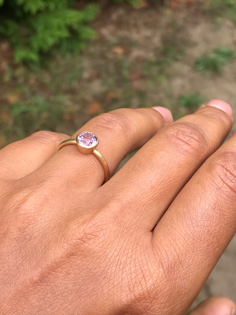 May include: A gold ring with a round, light purple gemstone.