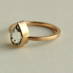 May include: A gold ring with a pear-shaped clear gemstone.