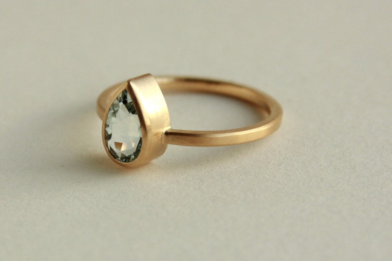 May include: A gold ring with a pear-shaped clear gemstone.