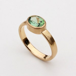 May include: A gold ring with a green oval gemstone set in a bezel setting.