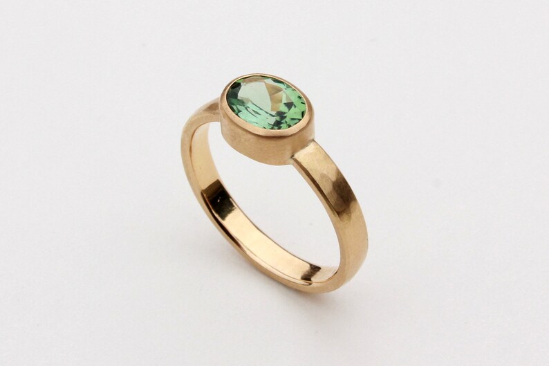 May include: A gold ring with a green oval gemstone set in a bezel setting.
