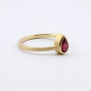 May include: A gold ring with a pear-shaped ruby gemstone.