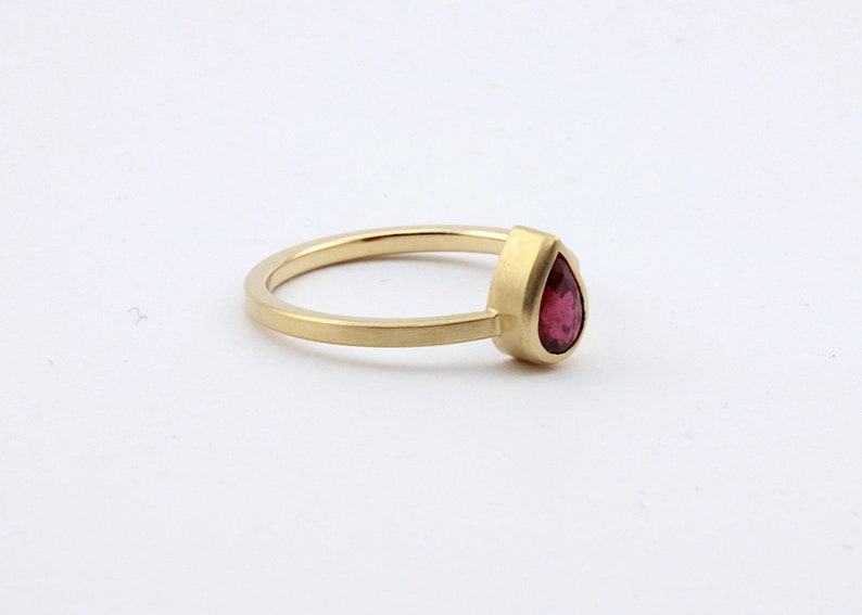 May include: A gold ring with a pear-shaped ruby gemstone.