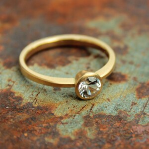 May include: A simple gold band ring with a single round clear gemstone set in a bezel setting.