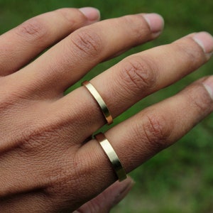 May include: Two gold-colored rings on a person's finger. The rings are simple and flat, with a smooth finish.