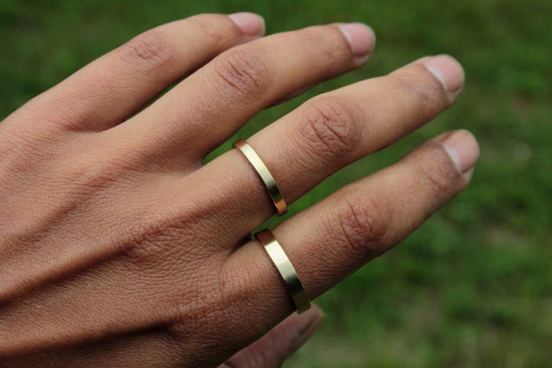 May include: Two gold-colored rings on a person's finger. The rings are simple and flat, with a smooth finish.
