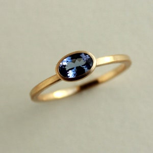 May include: A gold ring with a blue oval gemstone set in a bezel setting.