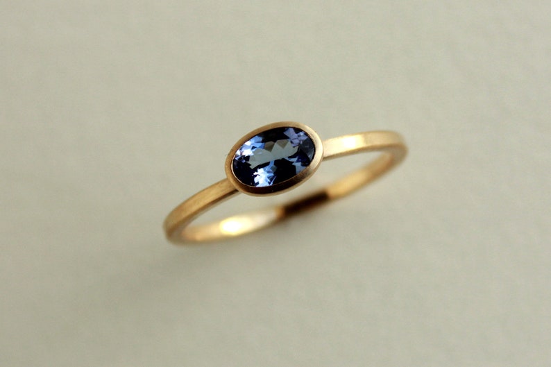 May include: A gold ring with a blue oval gemstone set in a bezel setting.