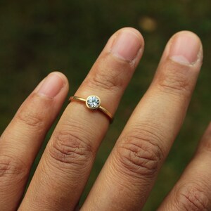 May include: A gold ring with a single, clear, round gemstone set in the center.