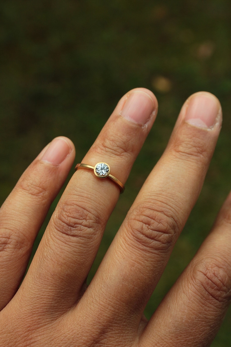 May include: A gold ring with a single, clear, round gemstone set in the center.