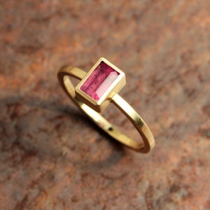 May include: A gold ring with a rectangular pink gemstone set in the center.