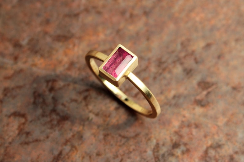 May include: A gold ring with a rectangular pink gemstone set in the center.