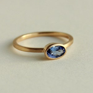 May include: A gold ring with a bezel setting featuring a blue oval gemstone.