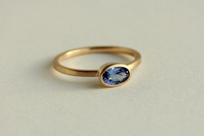 May include: A gold ring with a bezel setting featuring a blue oval gemstone.