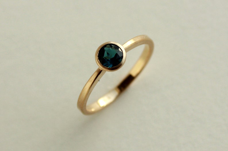 May include: A gold ring with a dark blue gemstone set in a bezel setting.