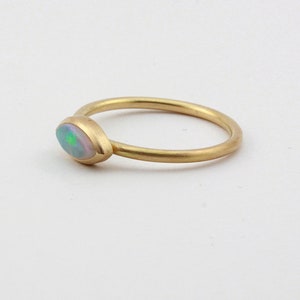 May include: A delicate gold ring with a single oval-shaped opal gemstone. The opal has a milky white base with flashes of green and blue.