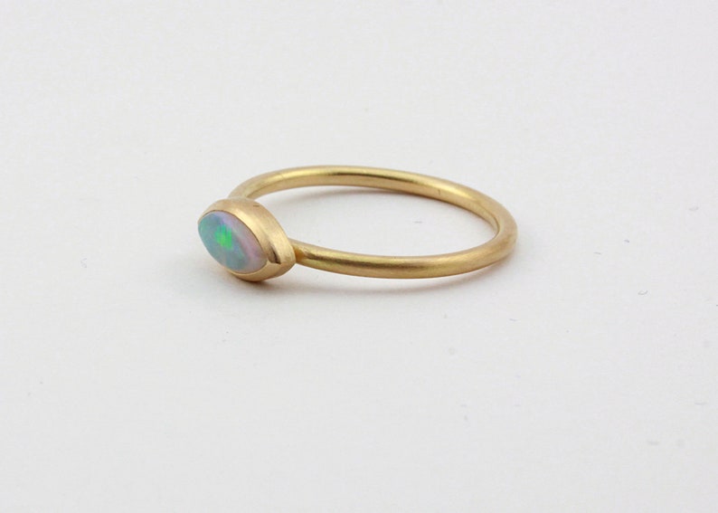 May include: A delicate gold ring with a single oval-shaped opal gemstone. The opal has a milky white base with flashes of green and blue.