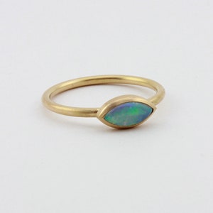 May include: A gold ring with a marquise-shaped opal gemstone. The opal is a light blue-green color with flashes of iridescent color.