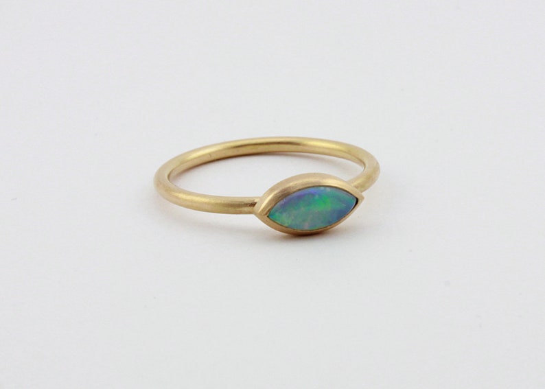 May include: A gold ring with a marquise-shaped opal gemstone. The opal is a light blue-green color with flashes of iridescent color.