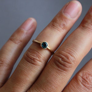May include: A gold ring with a small, round, dark blue gemstone.