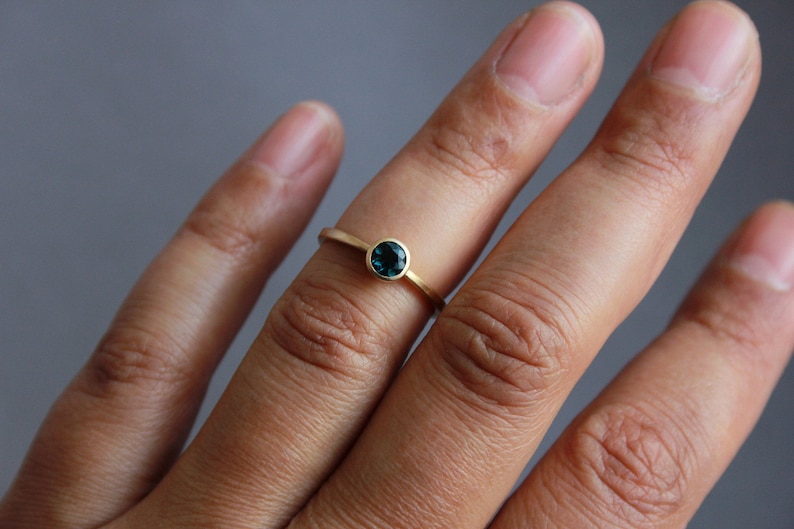 May include: A gold ring with a small, round, dark blue gemstone.