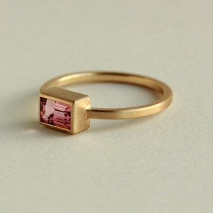 May include: A gold ring with a pink rectangular gemstone set in a bezel setting.