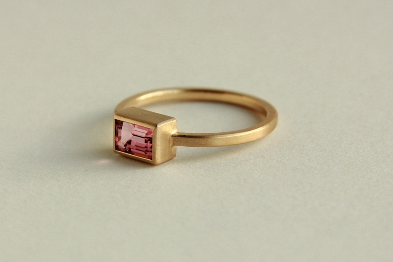 May include: A gold ring with a pink rectangular gemstone set in a bezel setting.
