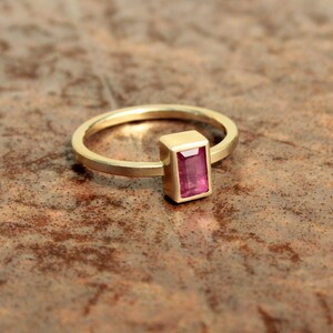May include: A gold ring with a rectangular pink gemstone set in a gold bezel.