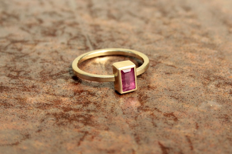 May include: A gold ring with a rectangular pink gemstone set in a gold bezel.