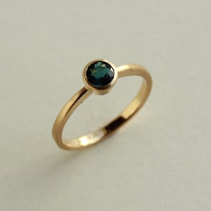 May include: A gold ring with a single round, dark blue gemstone.