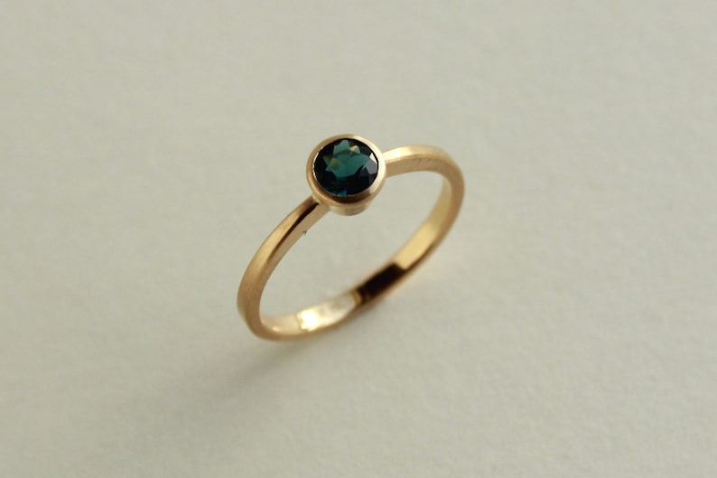 May include: A gold ring with a single round, dark blue gemstone.