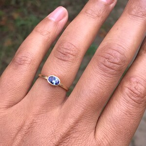 May include: A gold band ring with a small oval-shaped purple gemstone.