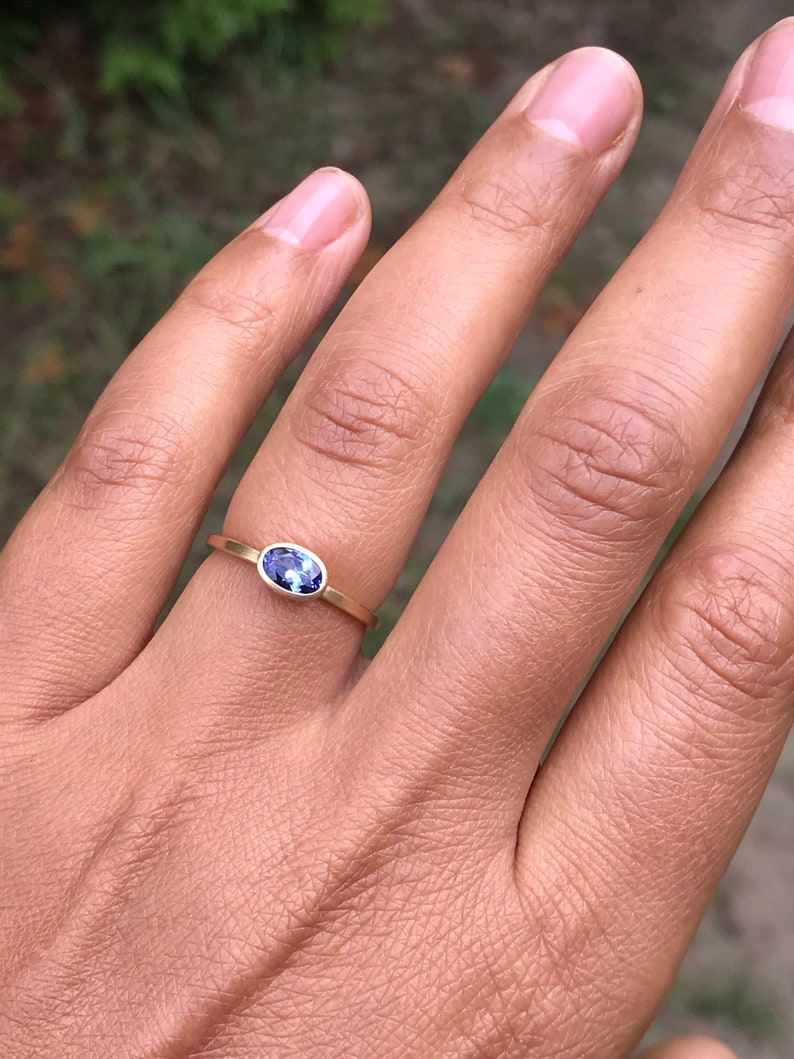 May include: A gold band ring with a small oval-shaped purple gemstone.