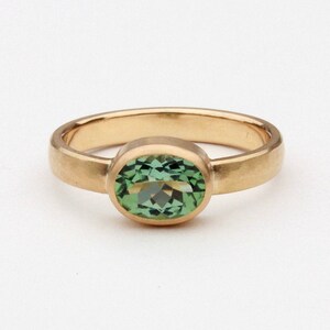 May include: A gold ring with a green oval gemstone set in a bezel setting.
