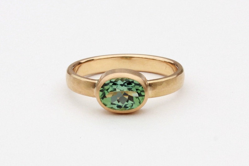 May include: A gold ring with a green oval gemstone set in a bezel setting.