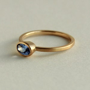 May include: A simple gold band ring with a small oval-shaped blue gemstone set in the centre.