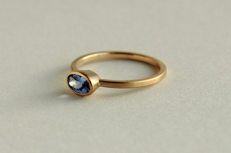 May include: A simple gold band ring with a small oval-shaped blue gemstone set in the centre.