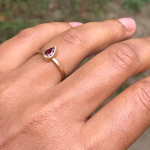 May include: A gold ring with a teardrop-shaped ruby gemstone.
