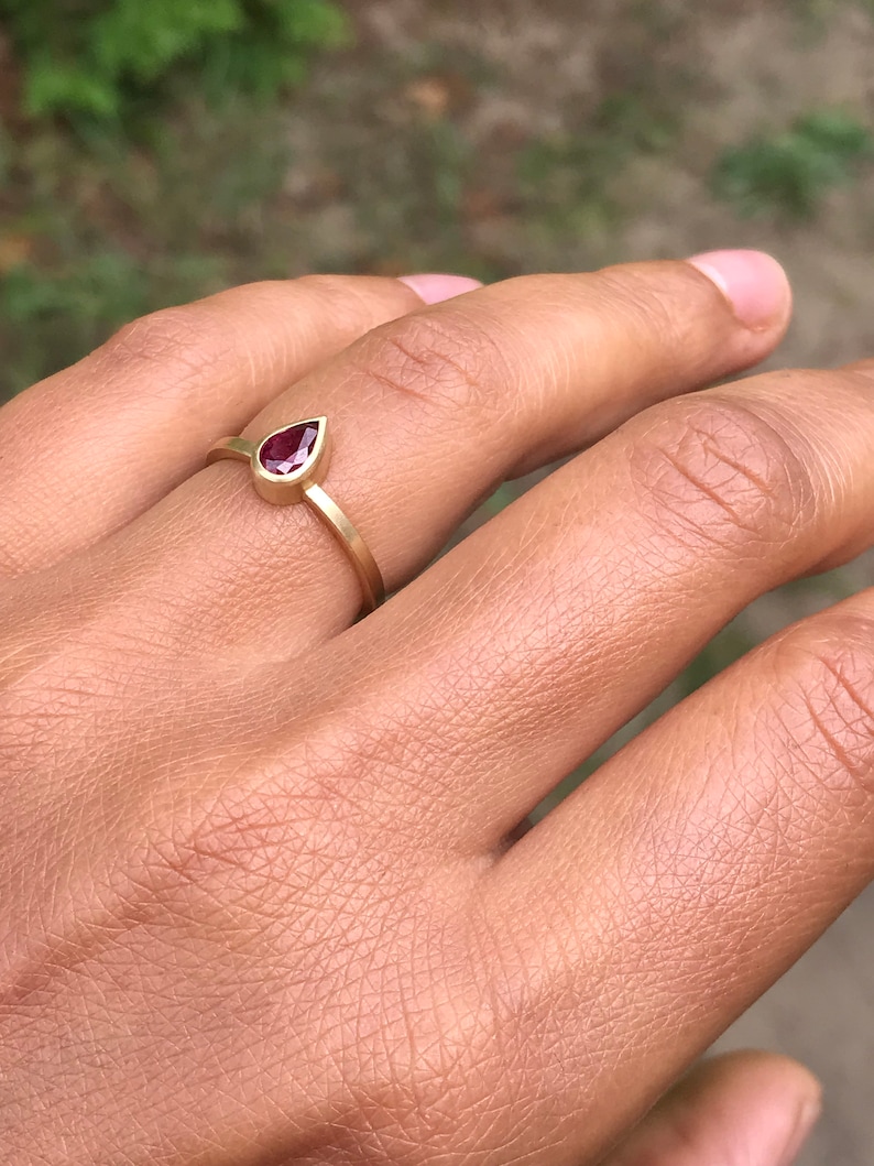 May include: A gold ring with a teardrop-shaped ruby gemstone.