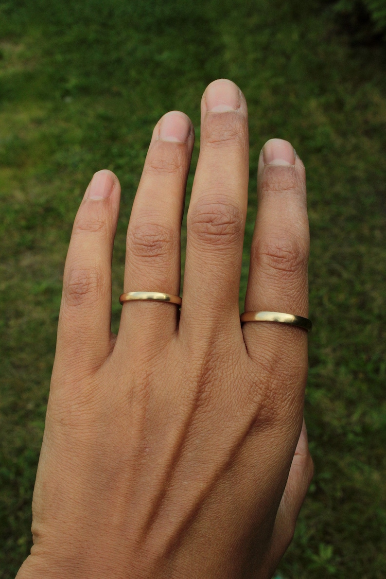 以下が含まれることがあります： 2つの金の結婚指輪をした手。指輪はシンプルでプレーンです