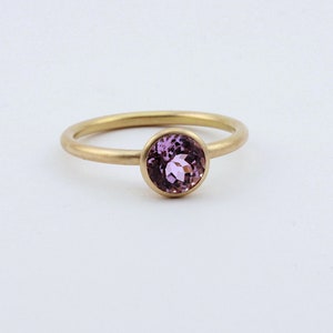 May include: A gold ring with a round, bezel-set, light purple gemstone.