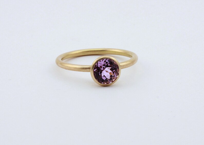 May include: A gold ring with a round, bezel-set, light purple gemstone.